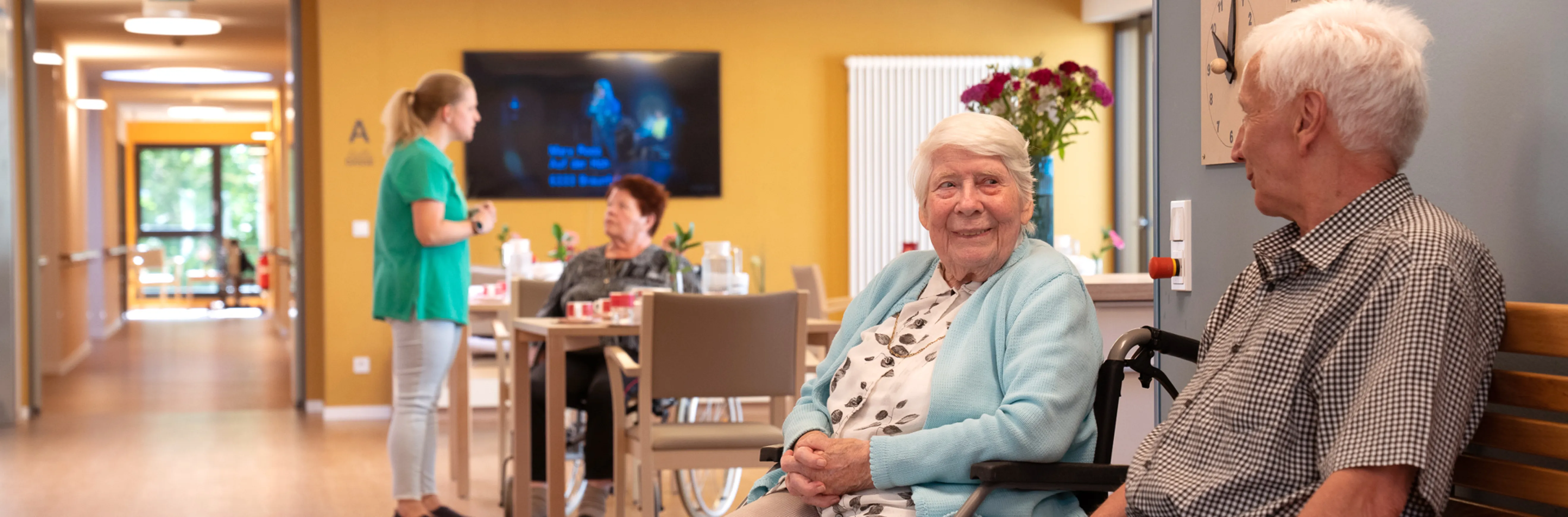 Zwei ältere Menschen die im Rollstuhl auf dem Flur Miteinander reden