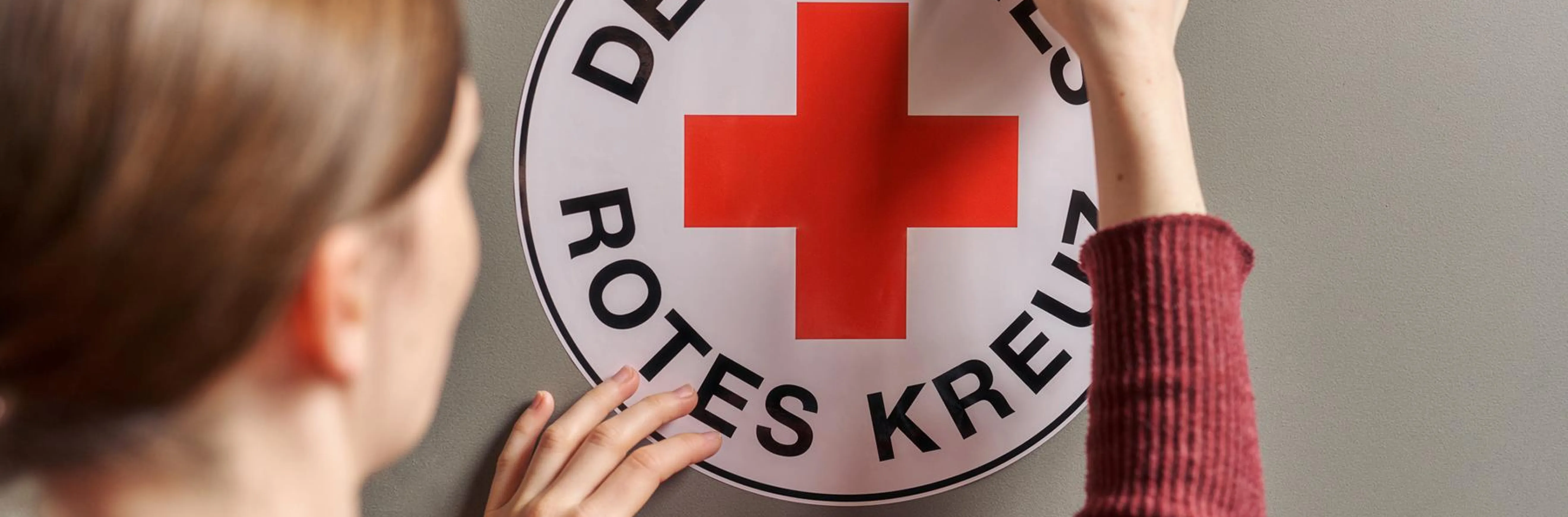 Eine Frau die das DRK Logo an eine Wand hängt 
